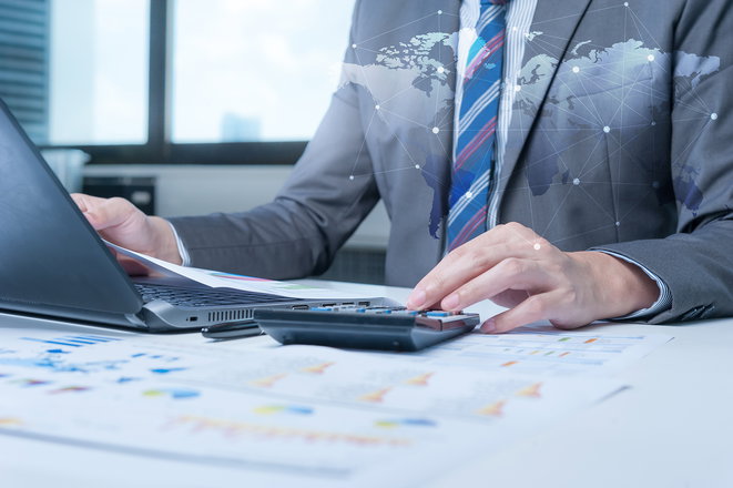 Closeup of businessman using laptop and calculator with creative business chart and map.